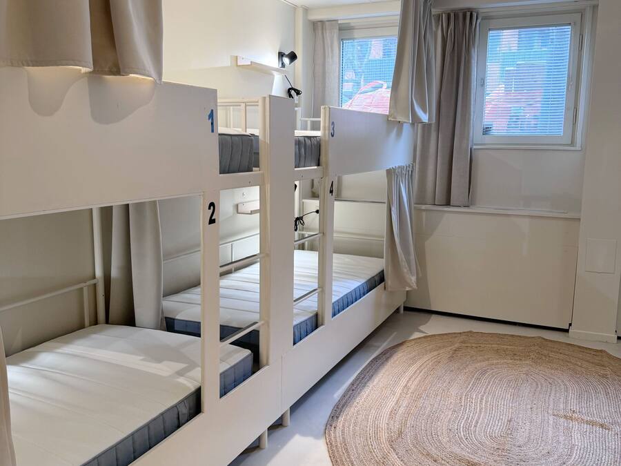 Une chambre avec des lits superposés, un tapis rond en fibres tressées et une fenêtre avec des stores.