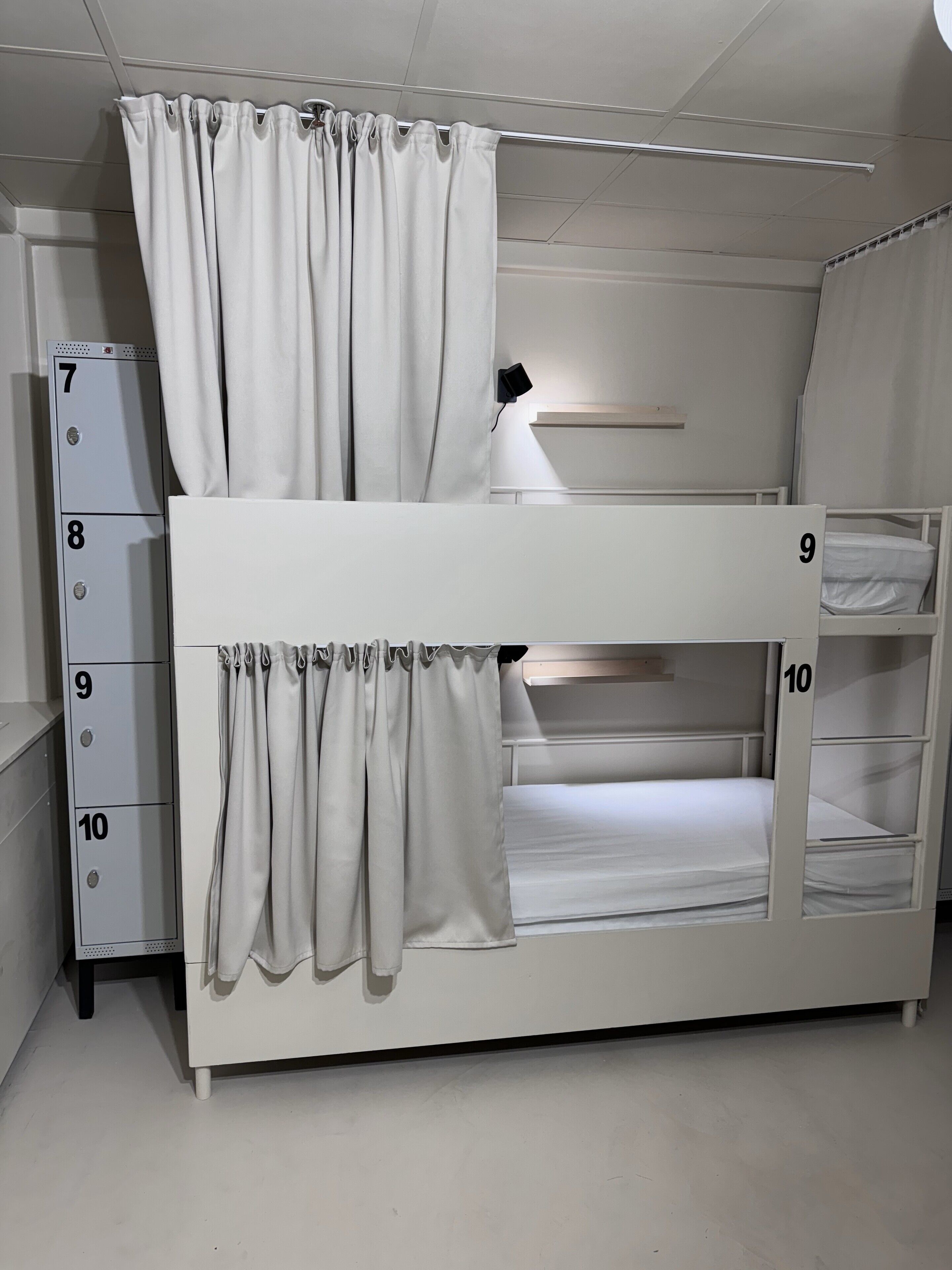 A bunk bed with numbers 9 and 10, a white wardrobe with numbers 7 to 10, and a desk with a lamp.