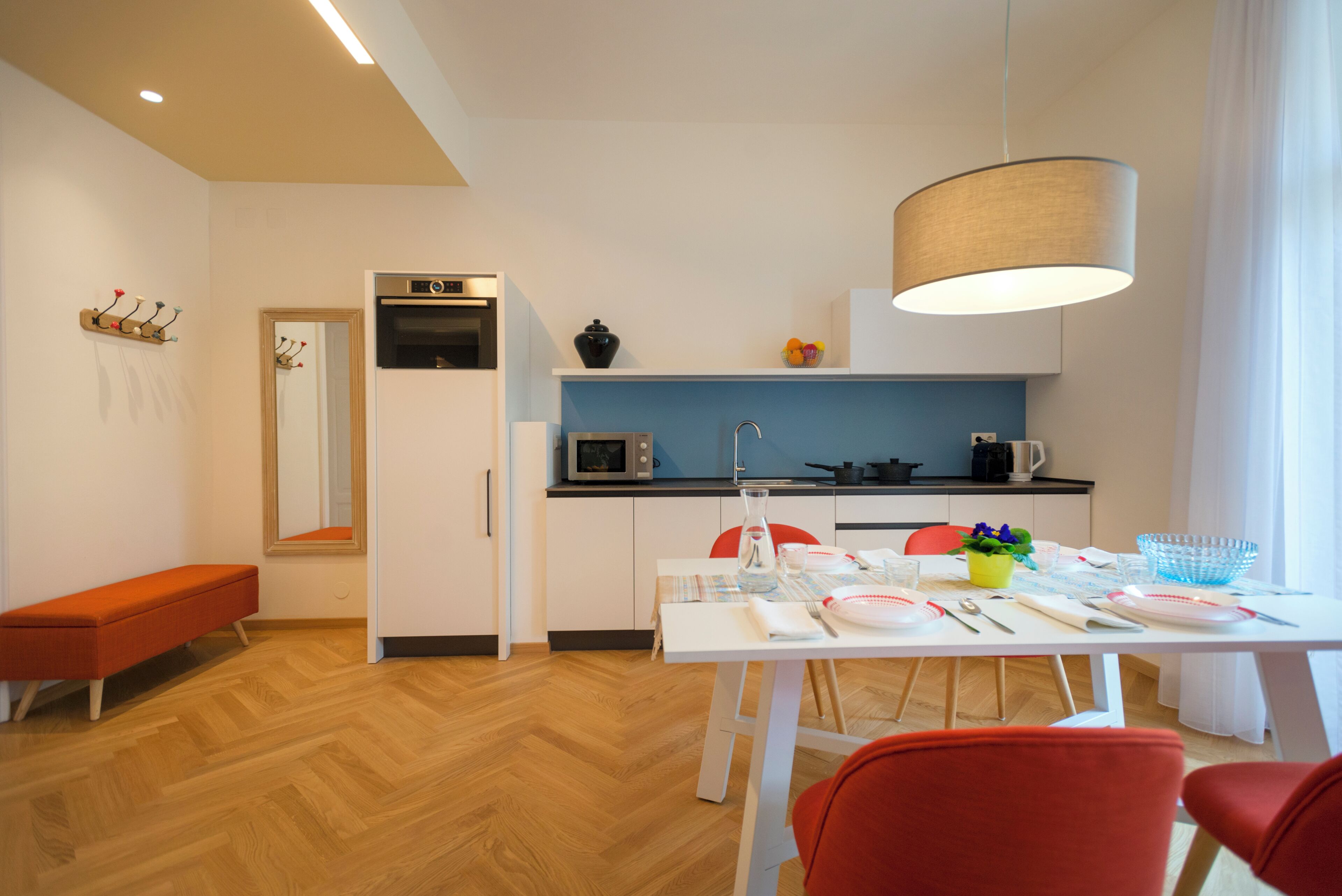 A modern kitchen with white cabinets, a microwave, and a coffee maker. There is a dining table with chairs and a bench.