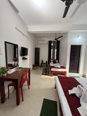 Une chambre d’hôtel avec deux lits, un bureau, une chaise, une télévision et un ventilateur de plafond.
