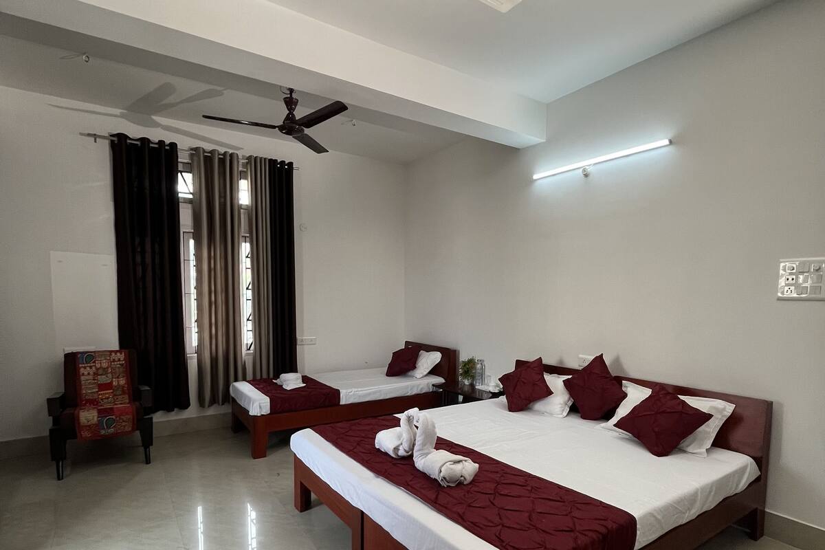 A hotel room with two beds, a ceiling fan, a bedside table, a chair, and a window with curtains.