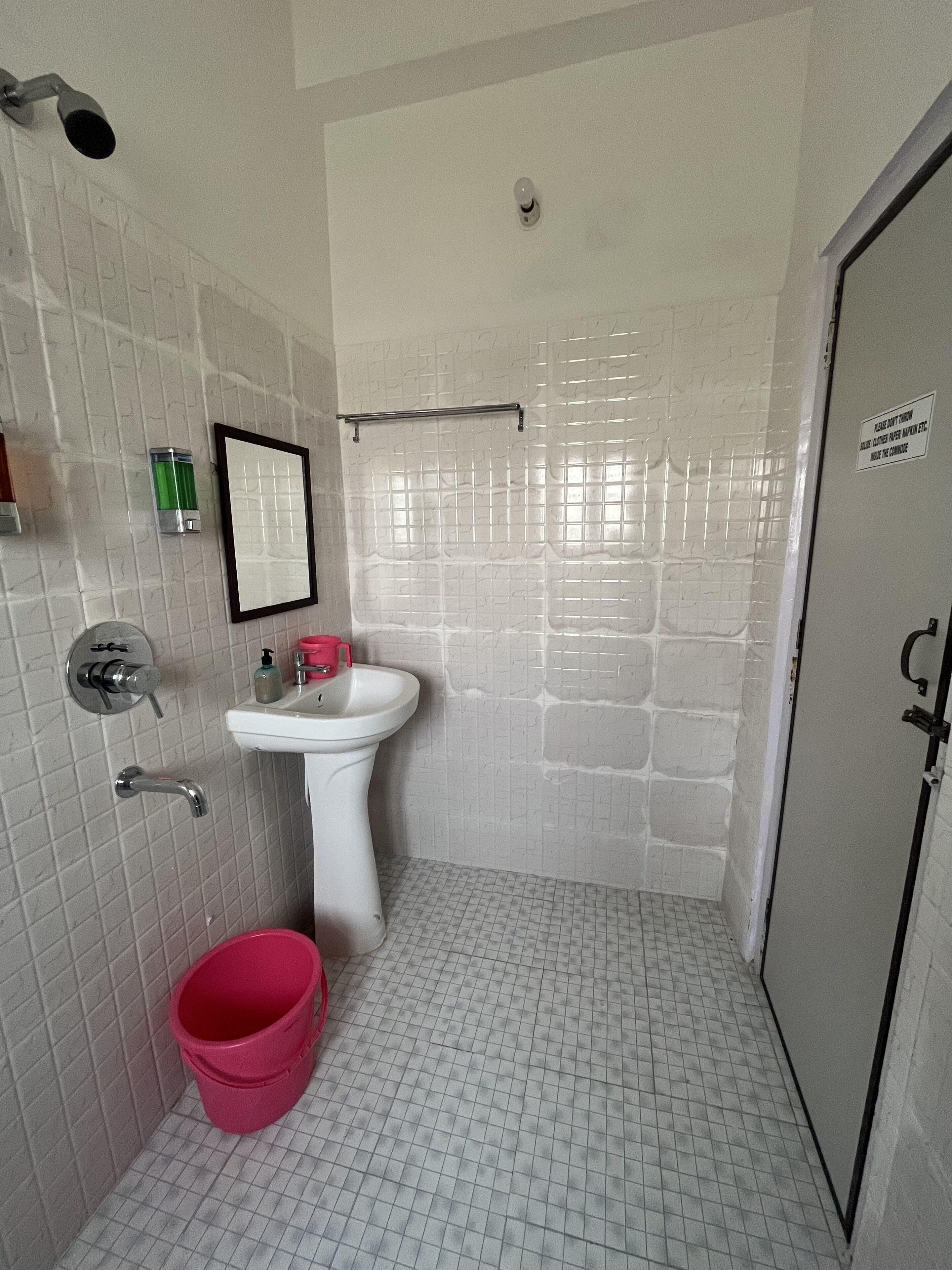 A small bathroom with a white sink, a mirror, a shower, and a door.