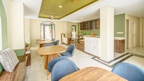 A spacious living area with a dining table, blue chairs, a sofa with a patterned cushion, a wooden bench, and a ceiling fan. - Habitat at Gandaria (Jakarta)