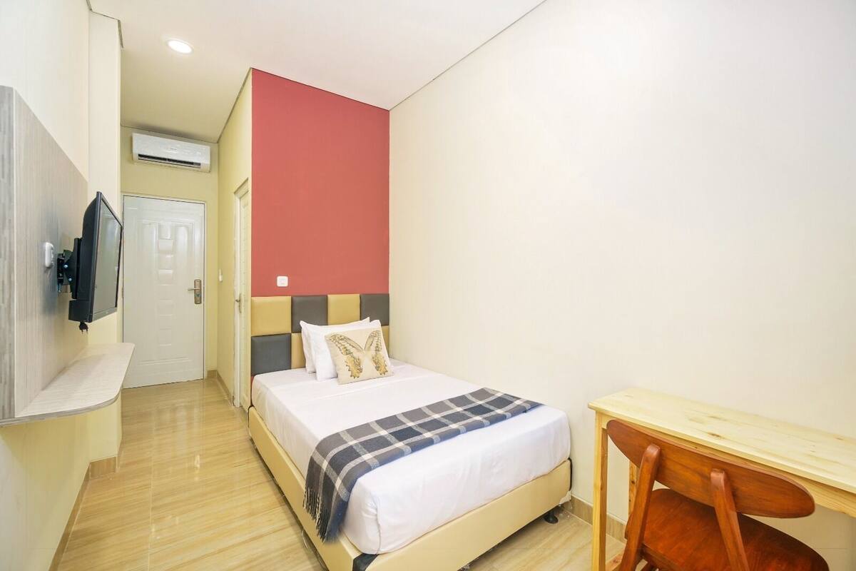 A hotel room with a bed, a TV mounted on the wall, a wooden desk, and a chair.