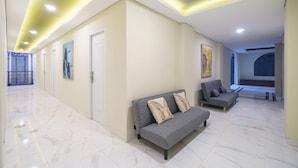 A modern interior with a hallway leading to a seating area, featuring a sofa and armchairs, a ceiling with recessed lighting, and a door with a window. - Habitat at Gandaria (Jakarta)