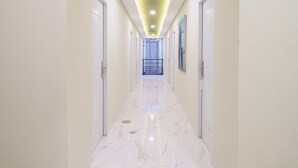 A long, narrow hallway with white walls and a marble floor, leading to a door at the end. - Habitat at Gandaria (Jakarta)