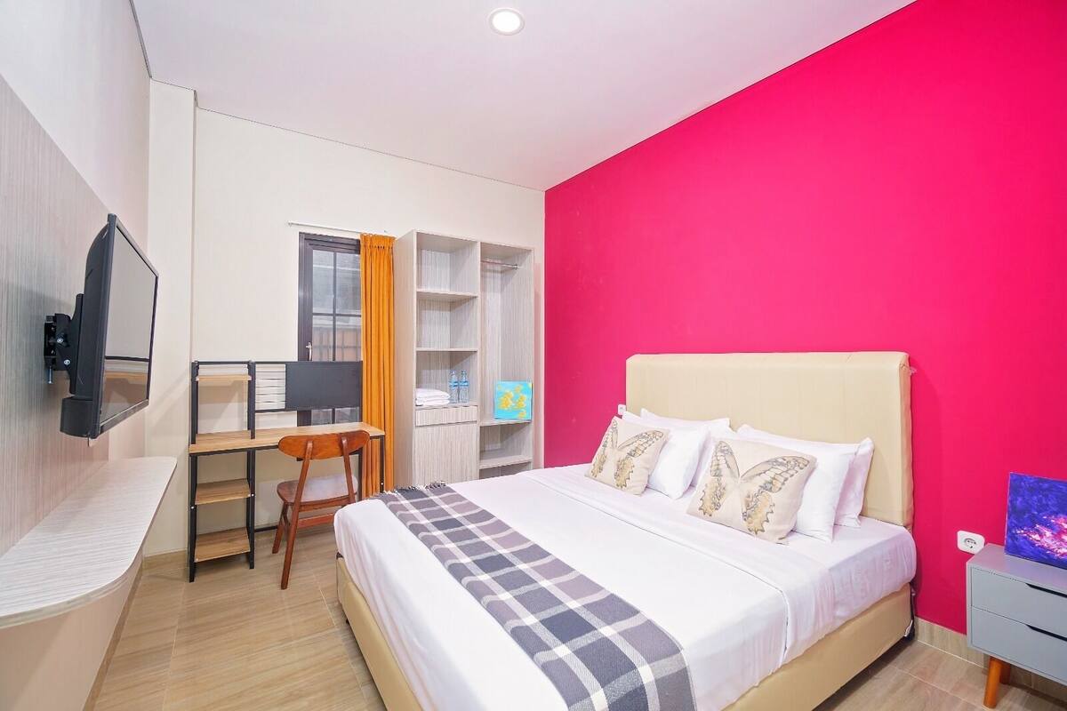 A hotel room with a bed, a desk, a chair, a TV, and a wardrobe.