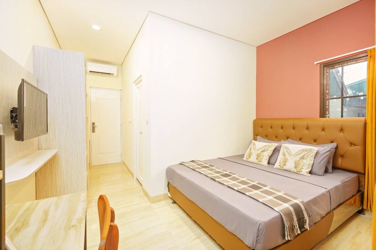 A bedroom with a bed, a TV, a desk, and a window.