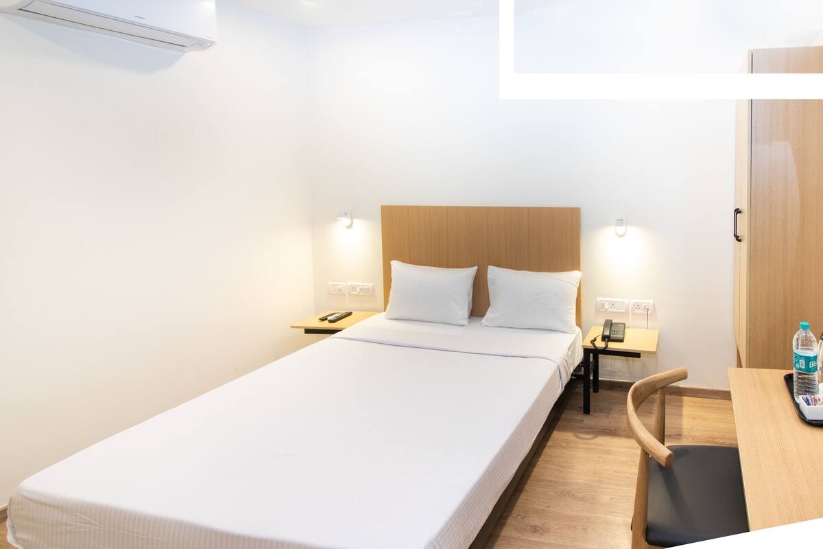 Una habitación de hotel con una cama individual, mesitas de noche, un escritorio con una silla y un armario.
