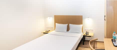 Una habitación de hotel con una cama individual, mesitas de noche, un escritorio con una silla y un armario.