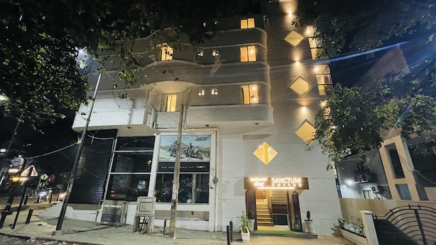 Ein mehrstöckiges Hotel mit modernem Design, das einen markanten Eingangsbereich mit einer Treppe und einem Schild für 'Sanctum Suites' zeigt.
