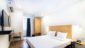Ein Hotelzimmer mit einem großen Bett, einem Schreibtisch mit Stuhl, einem an der Wand montierten Fernseher und einem Holzschrank.