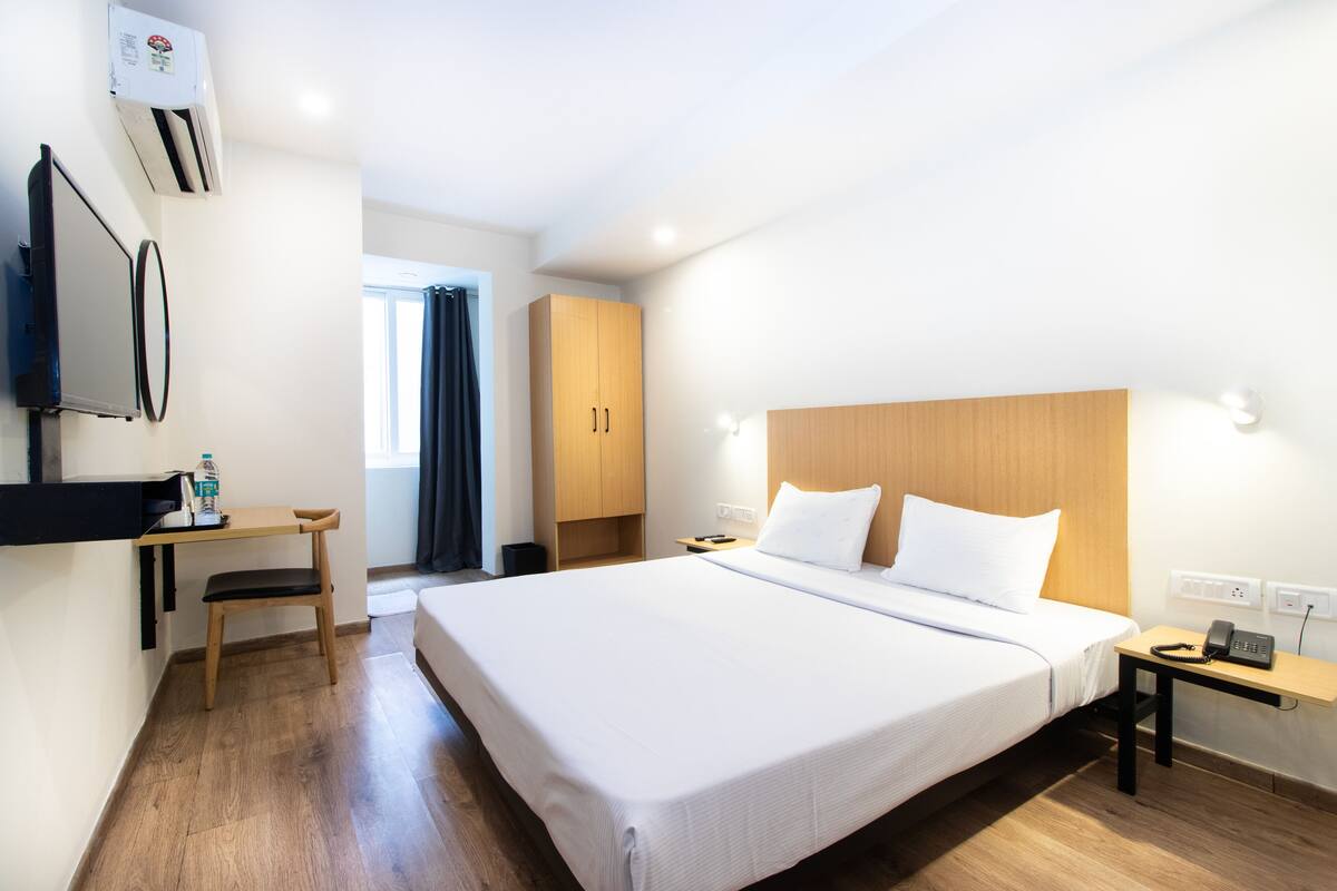 Habitación de hotel con una cama grande, un escritorio con silla, un televisor montado en la pared y un armario de madera.