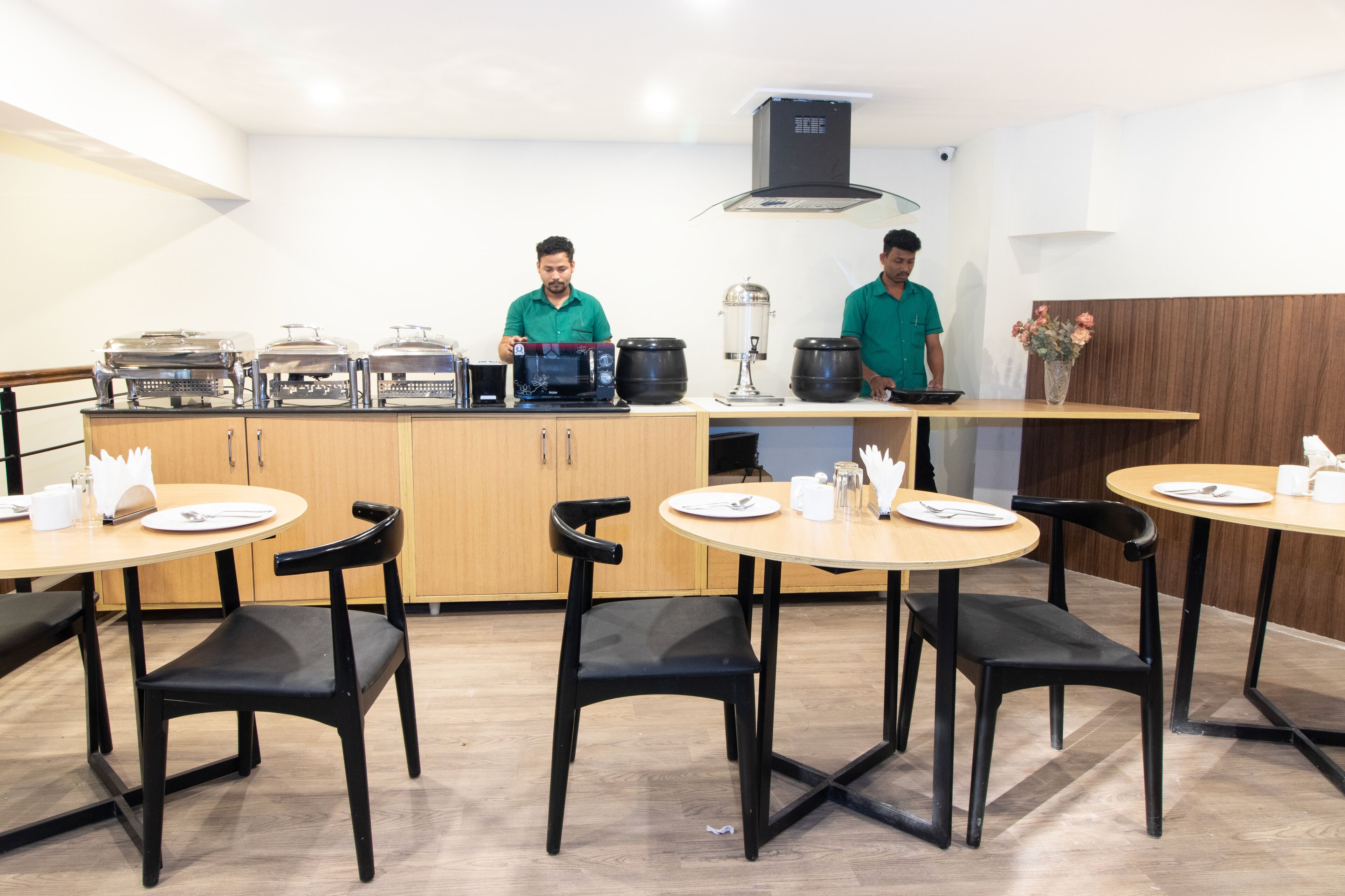 A modern kitchen with two chefs, buffet setup, and dining area with chairs and tables.