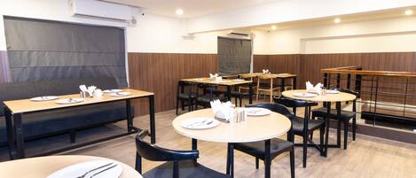 A dining area with round tables and black chairs, equipped with white plates and cutlery.