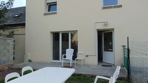 Un edificio de dos pisos con un patio que incluye una mesa, sillas, una ventana pequeña y una puerta.
