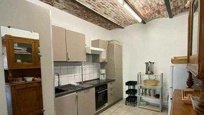 Una cocina compacta con piso de baldosas, gabinetes de madera, horno empotrado y cafetera.