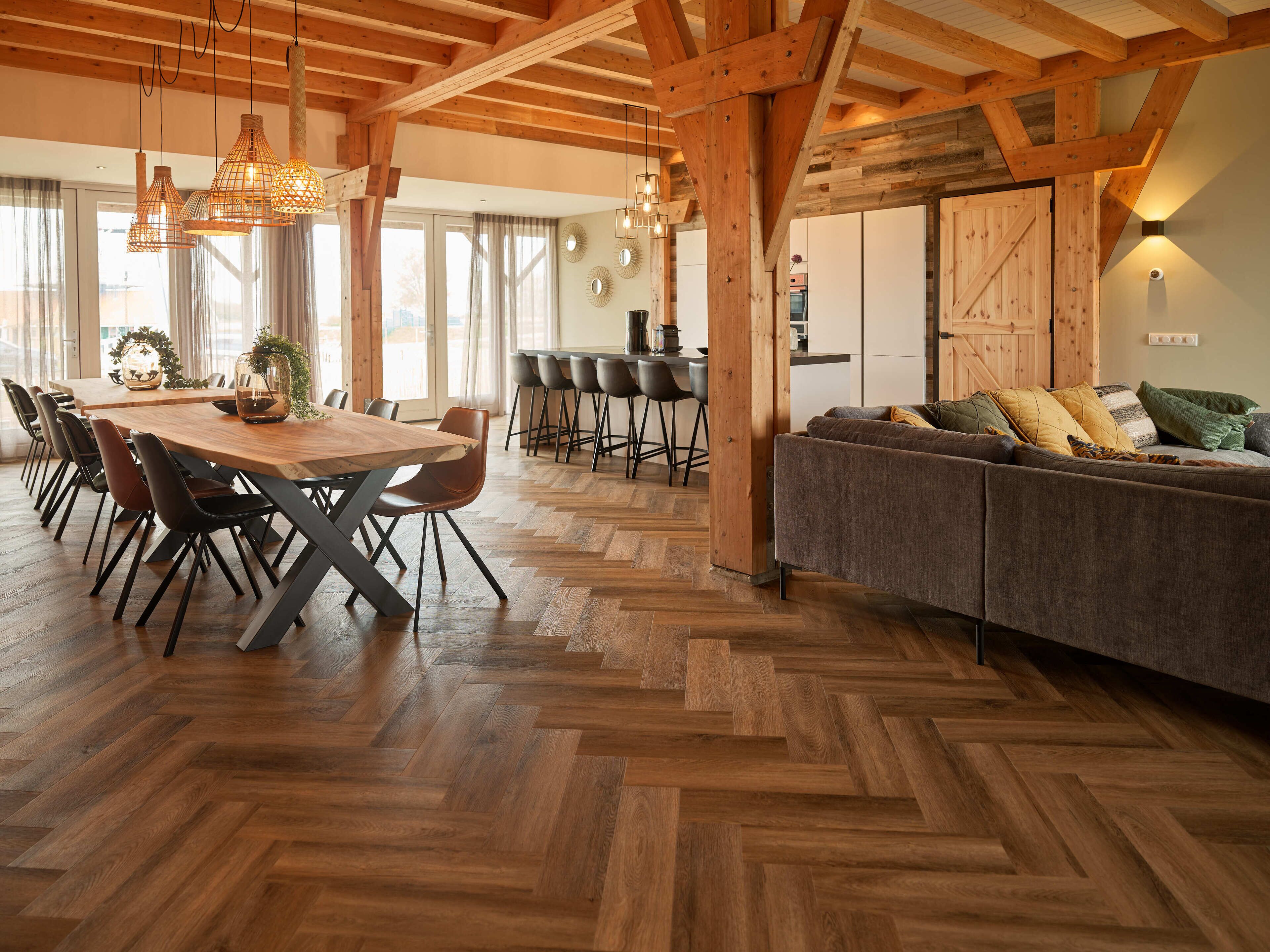 Ein geräumiger Essbereich mit Holztisch und -stühlen, einem Fischgrätparkett und einer gemütlichen Sitzecke mit Sofa und Kissen.