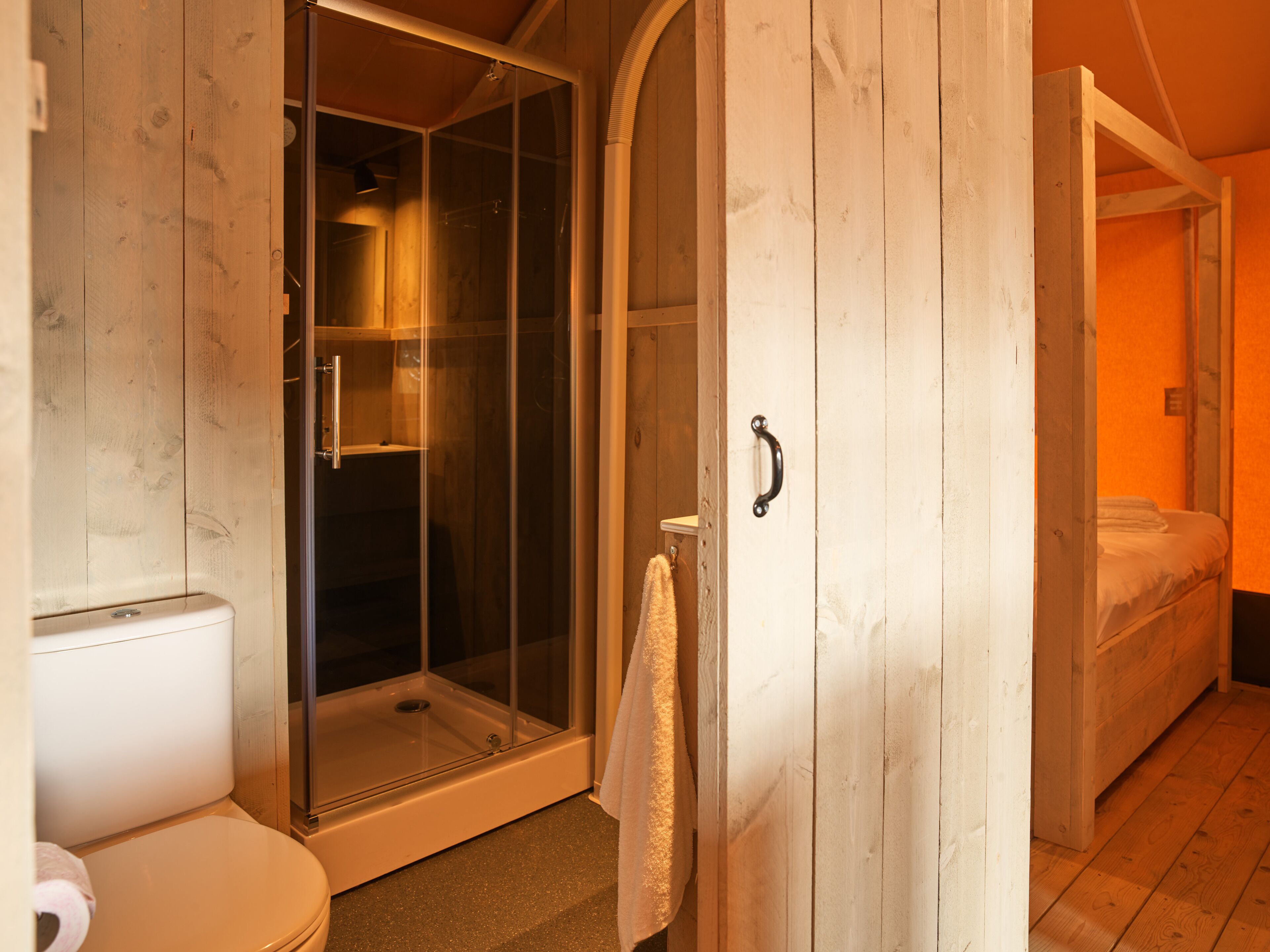 A wooden room with a shower, toilet, and a bed.