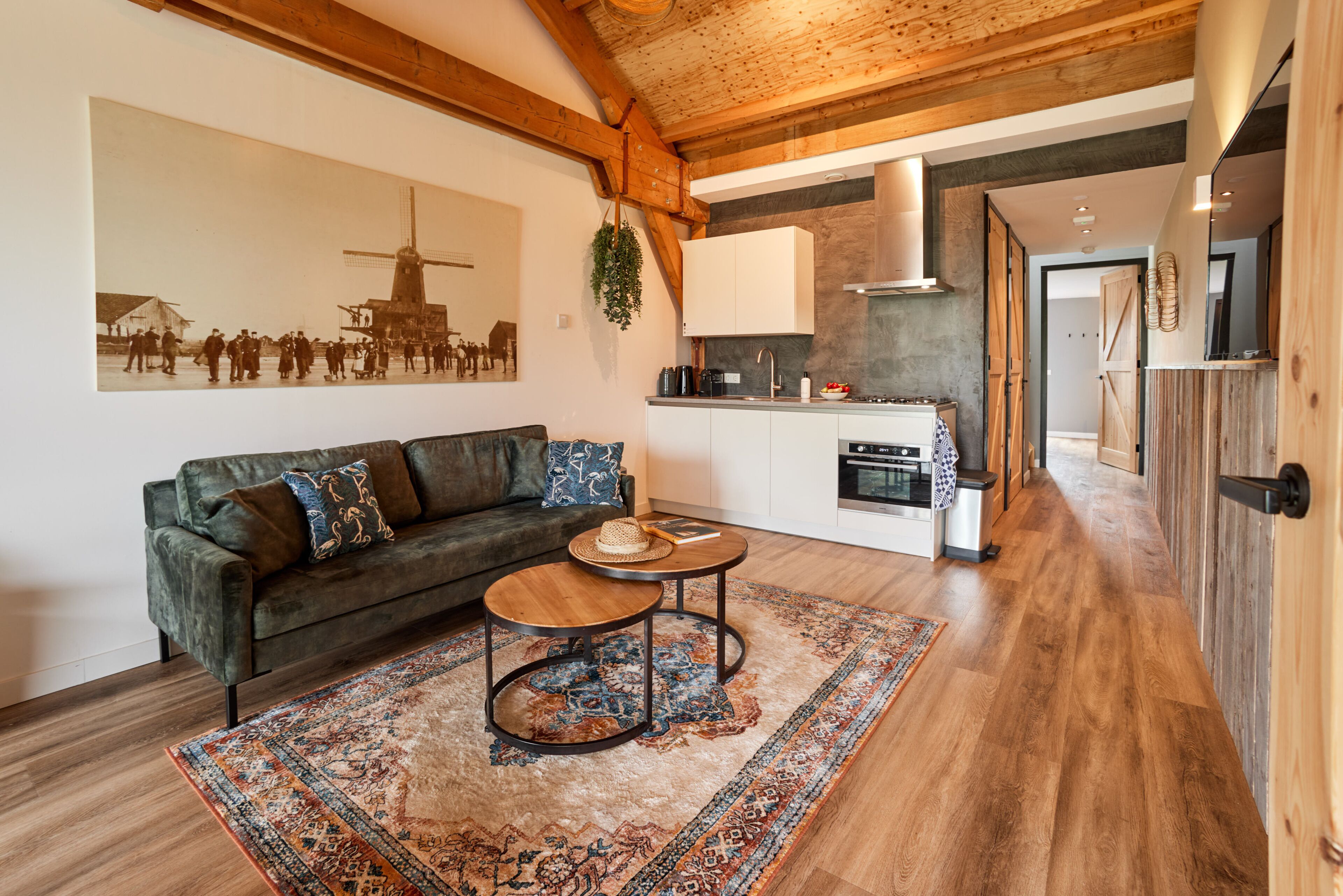 Un salon chaleureux avec un canapé, une table basse et un tapis. On aperçoit, au fond, une cuisine équipée d’appareils électroménagers modernes.