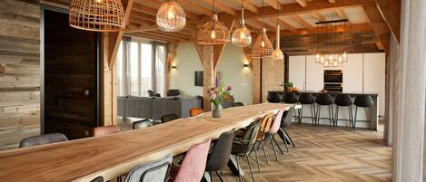 A spacious dining area with a long wooden table, multiple chairs, and hanging pendant lights.
