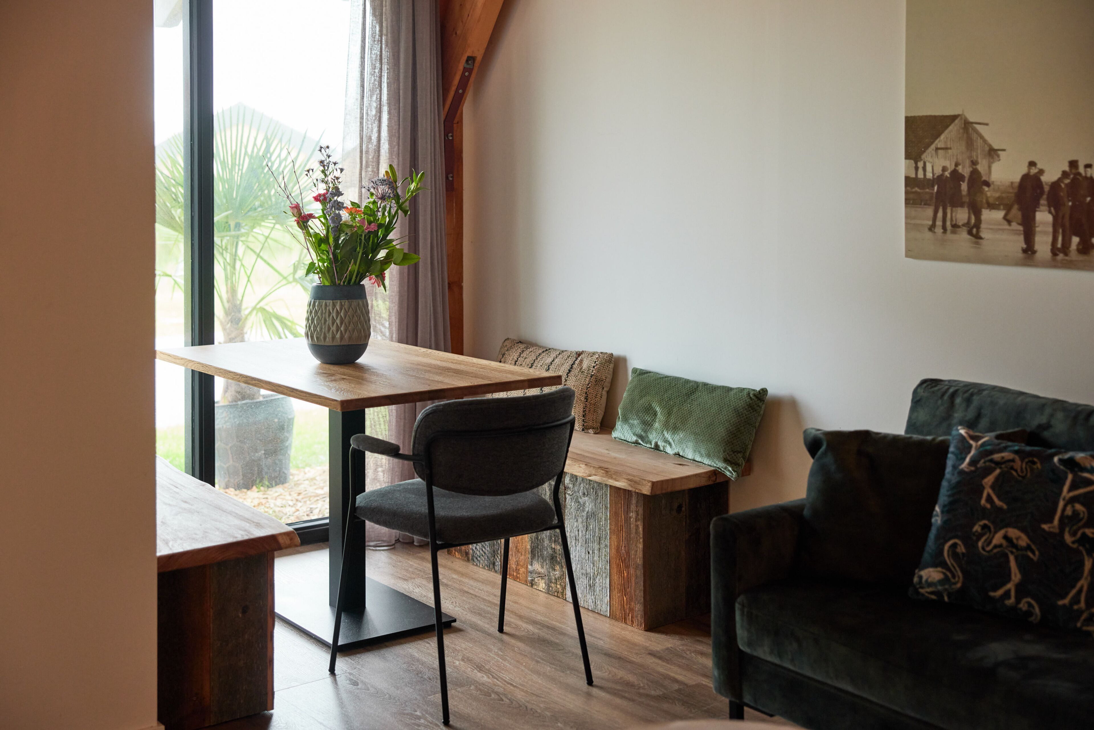 Une pièce chaleureuse avec une table en bois, une chaise gris foncé, un coussin vert sur un banc en bois et un canapé vert foncé agrémenté de coussins à motifs.