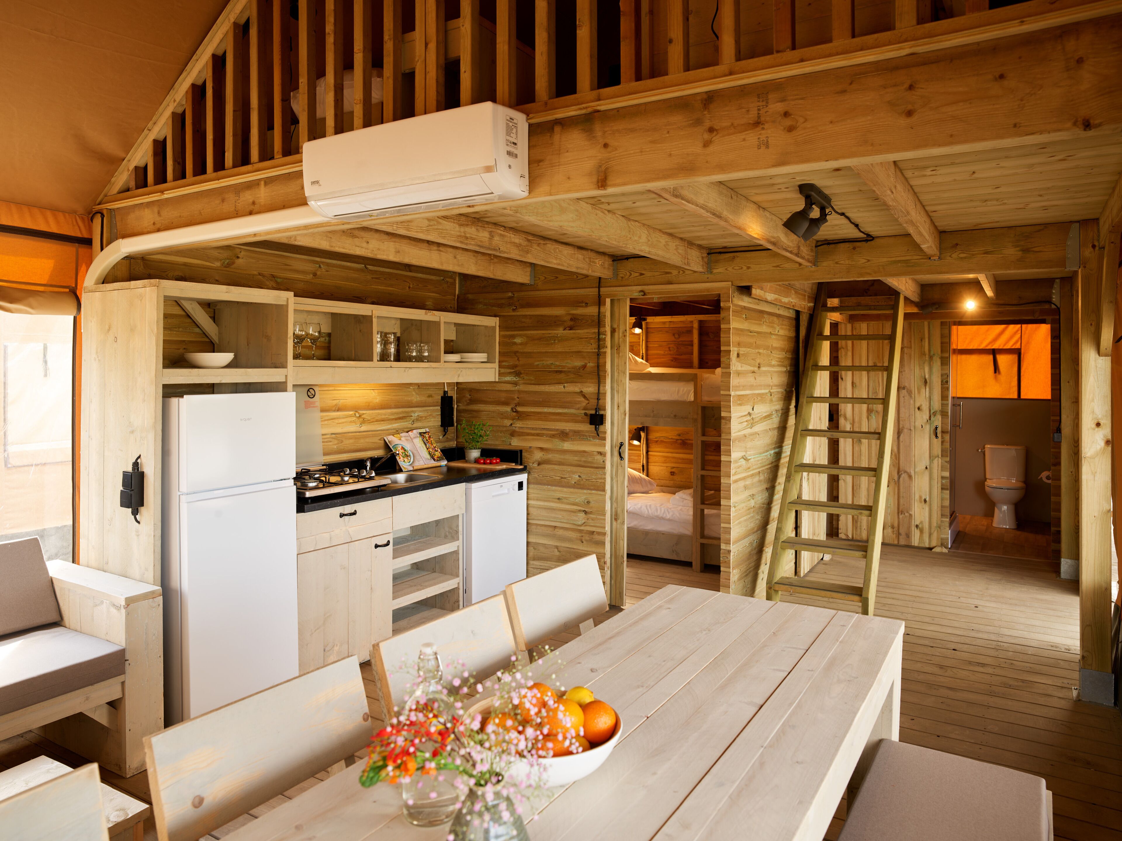 A wooden cabin interior with a kitchen, dining area, and a sleeping loft.