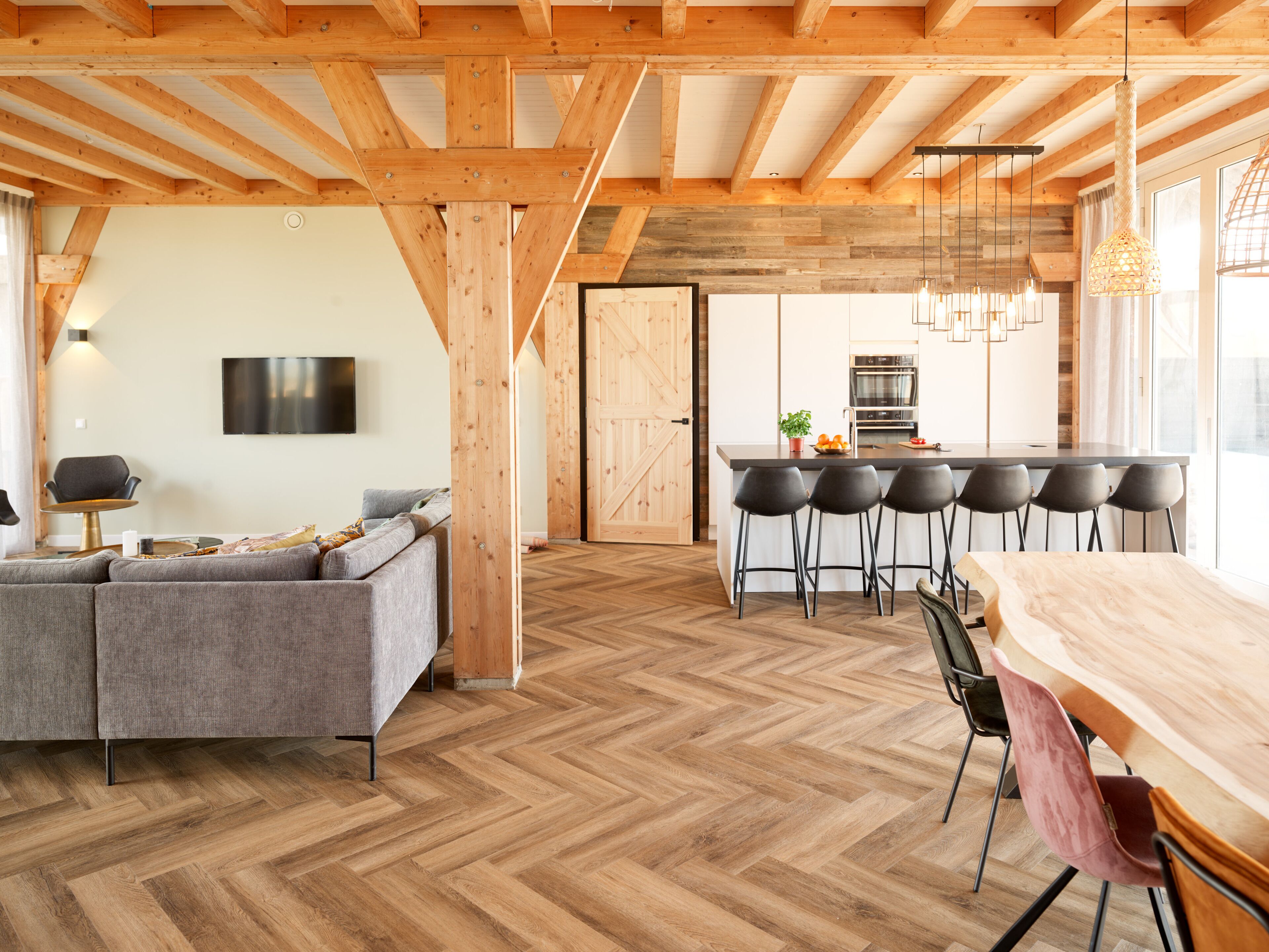 Ein geräumiger Wohnbereich mit Fischgrätparkett, einem grauen Sofa und einem Holzesstisch mit sechs Stühlen.