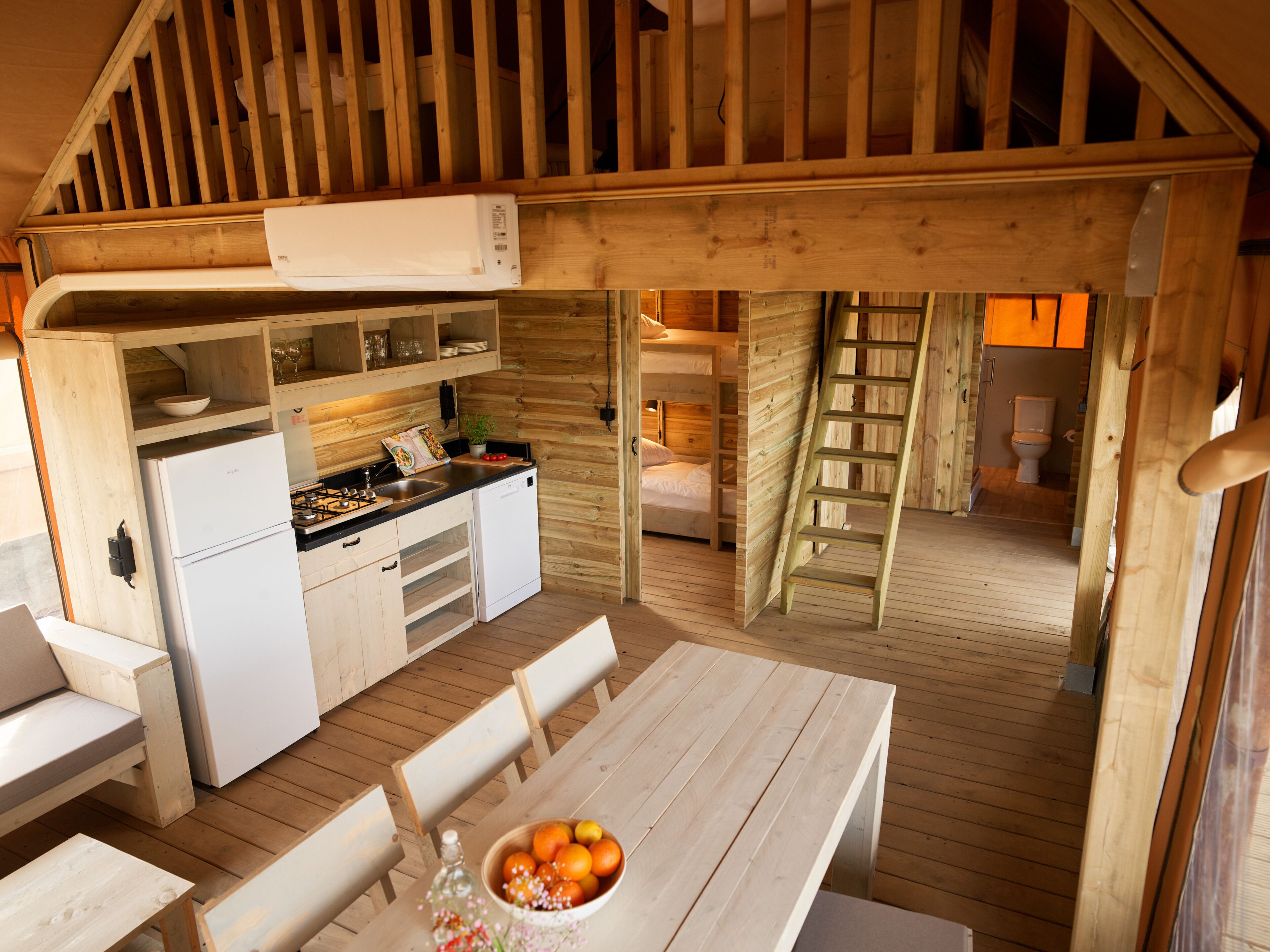 Una cabaña de madera compacta con una zona de cocina, una mesa de comedor con sillas y un altillo para dormir.