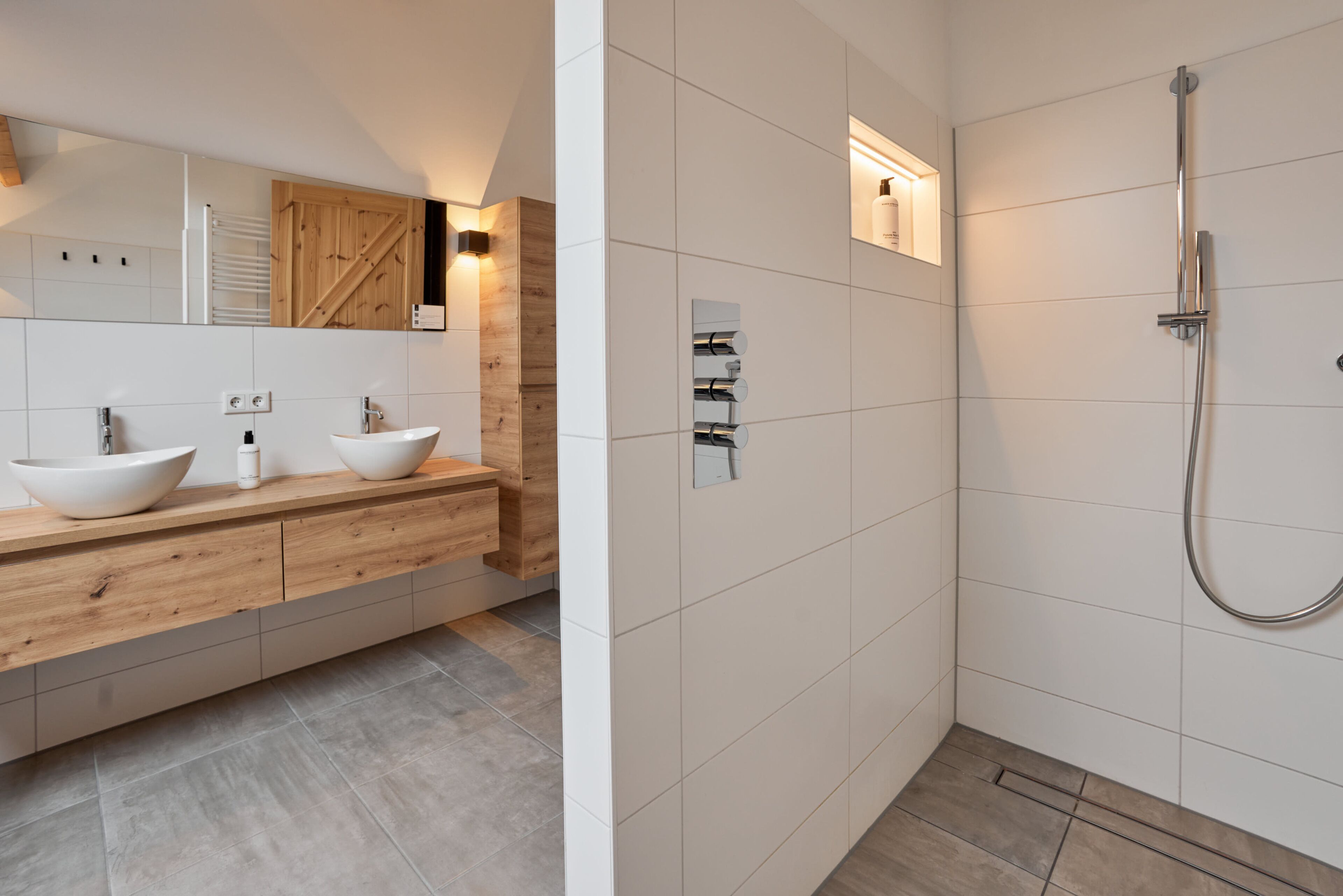 Een moderne badkamer met een houten wastafel, twee wasbakken, een grote spiegel en een douchegedeelte.