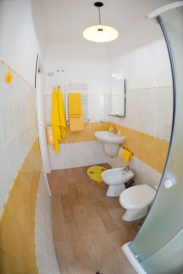 Un baño con lavamanos, bidé e inodoro. Toallas amarillas cuelgan de la pared.