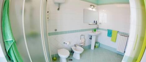 A bathroom with a shower, toilet, bidet, and sink.