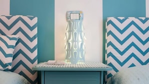 Ein Zimmer mit einem Bett, einem kleinen Tisch mit Lampe und einer Wand mit Zickzackmuster.