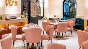 A modern dining area with pink upholstered chairs, a wooden buffet, and a green sofa. - Playsales Scarlet (Indore)