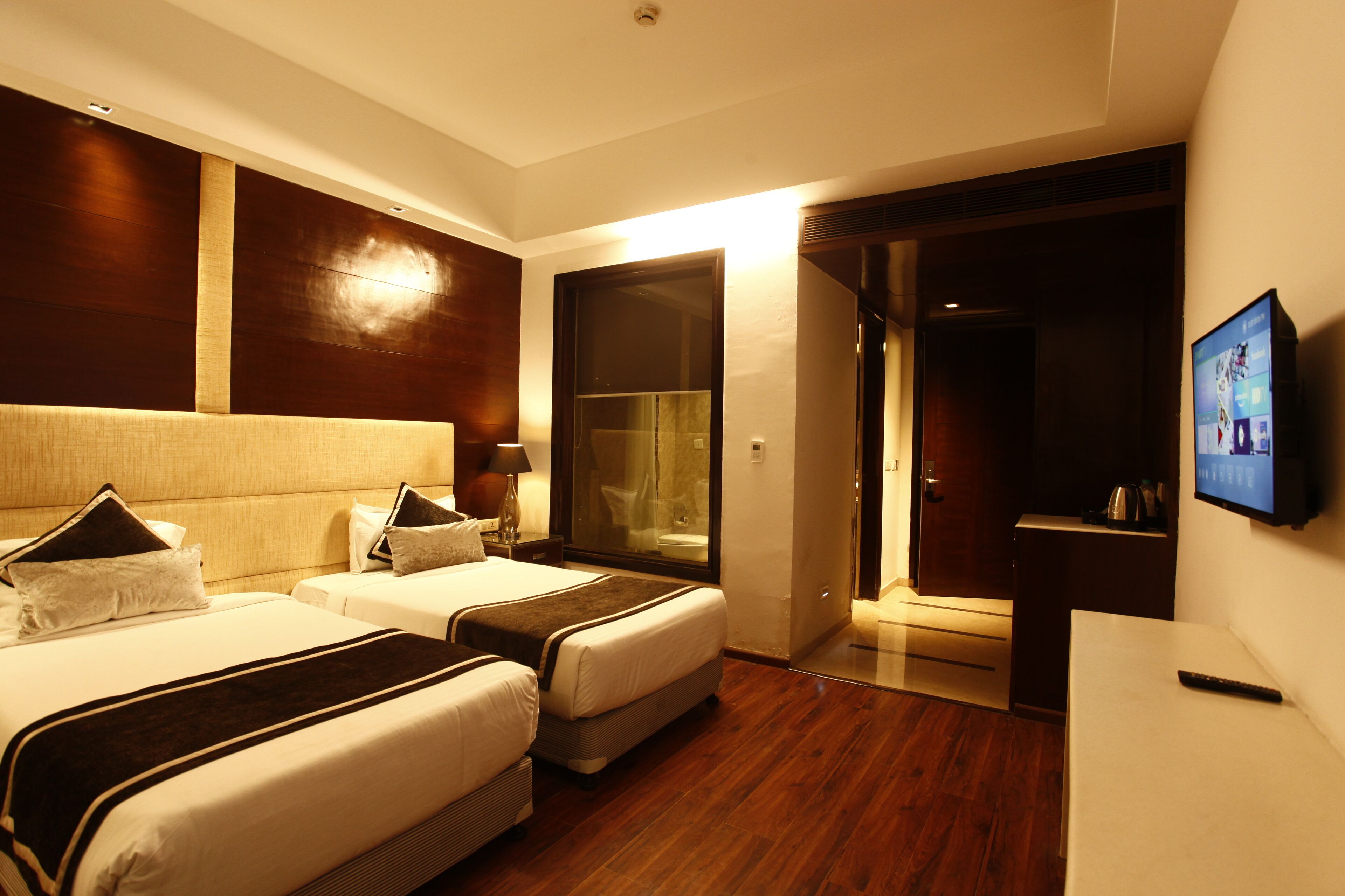 A hotel room with two beds, a television, and a bathroom visible through a glass door.