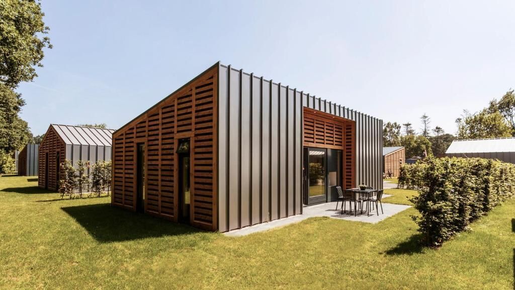 Een modern gebouw met een schuin dak, grote ramen en een patio met terrasmeubels.