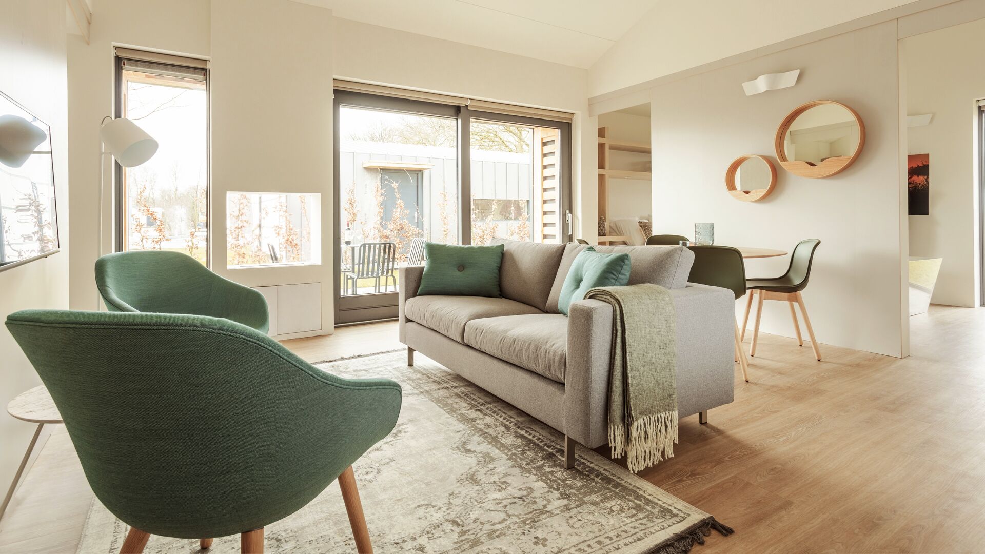 A modern living room with a sofa, two armchairs, a dining table, and a large window.