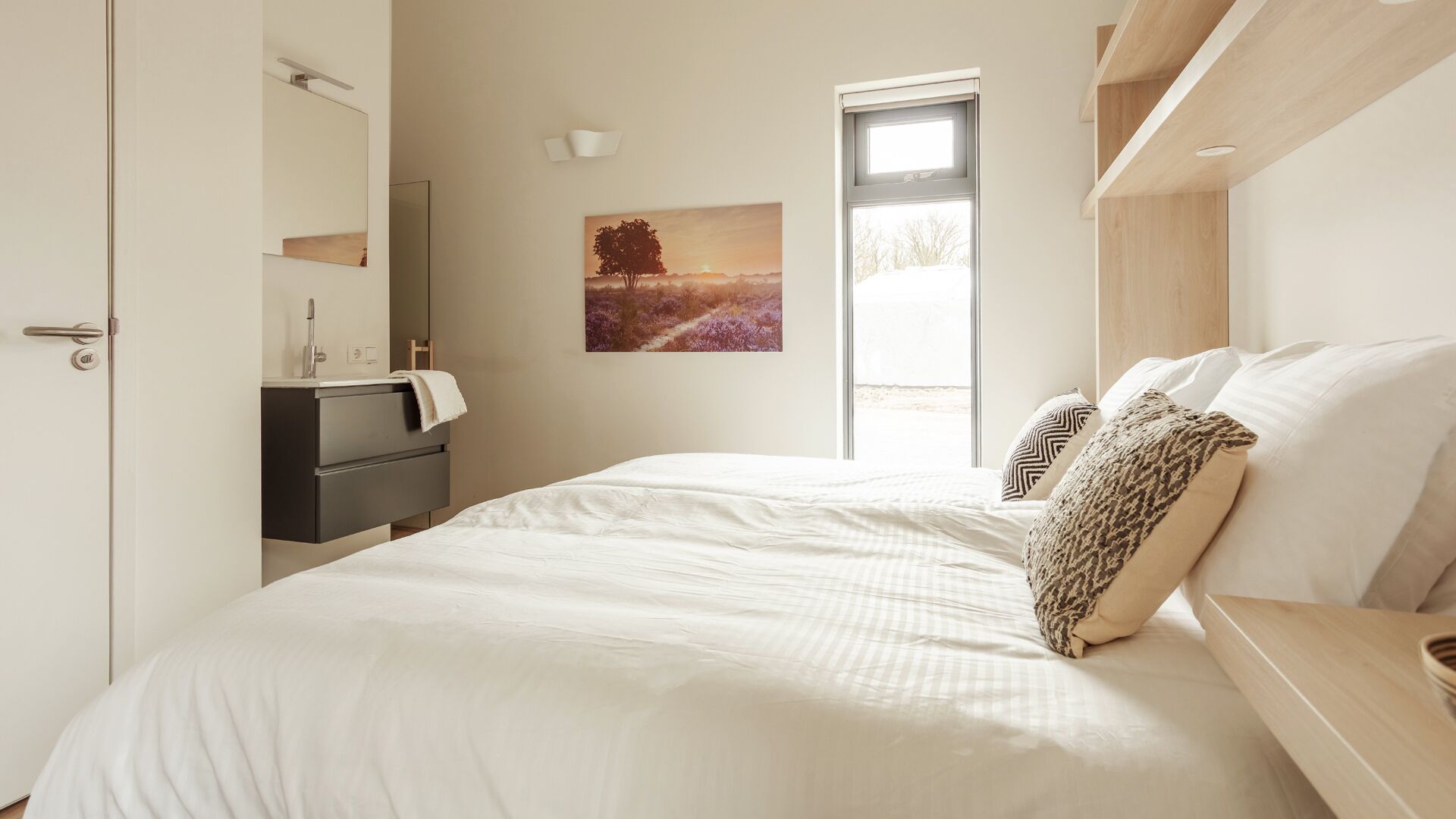 Une chambre à coucher avec un lit, une table de chevet, une commode, une fenêtre et un tableau au mur.