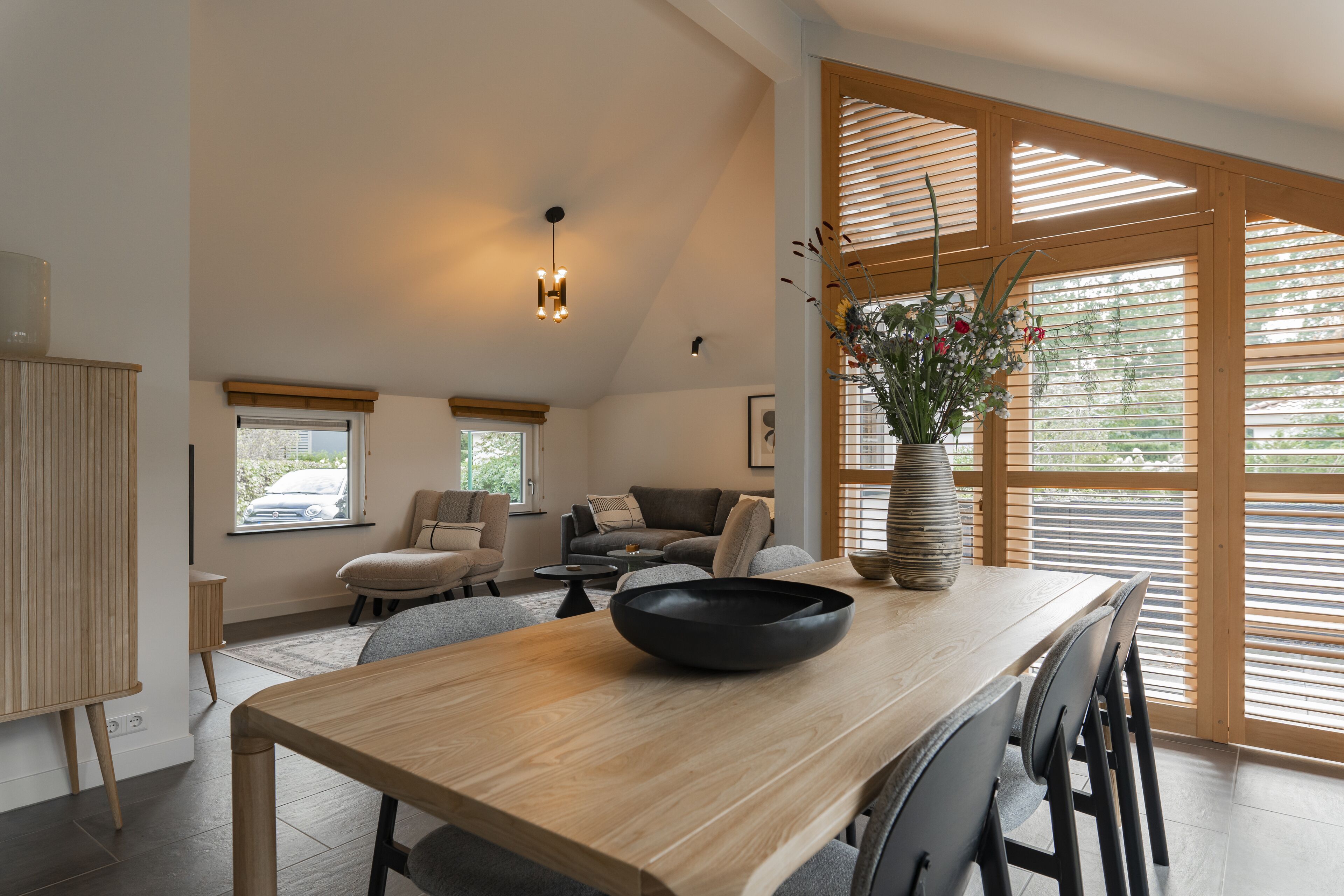 A spacious living area with a wooden dining table, a sofa, and a large window with blinds.