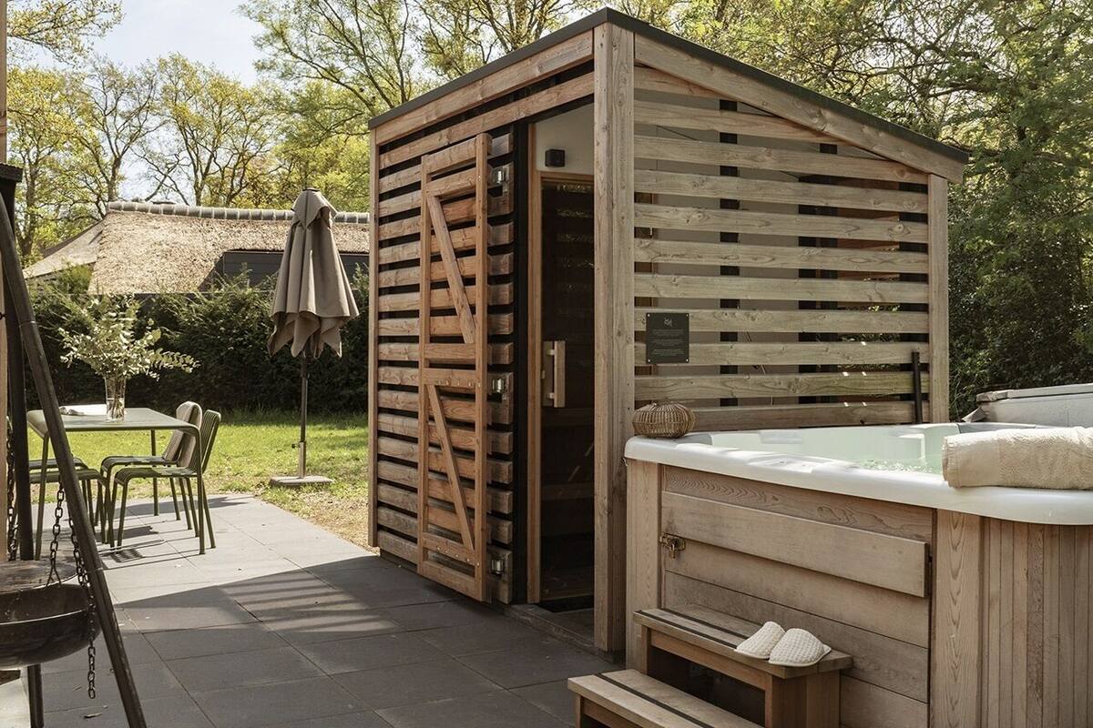 Un espace extérieur aménagé avec un bain à remous en bois, une structure en bois, une table avec des chaises et une échelle.
