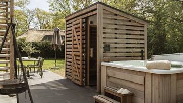 Een houten kuub voor een hottub buiten, met een houten constructie, een tafel en stoelen, en een trap.