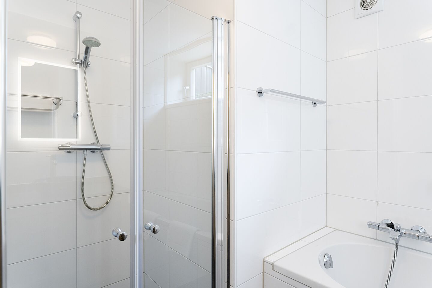 A modern bathroom with a glass shower enclosure, a separate bathtub, and a glass door.