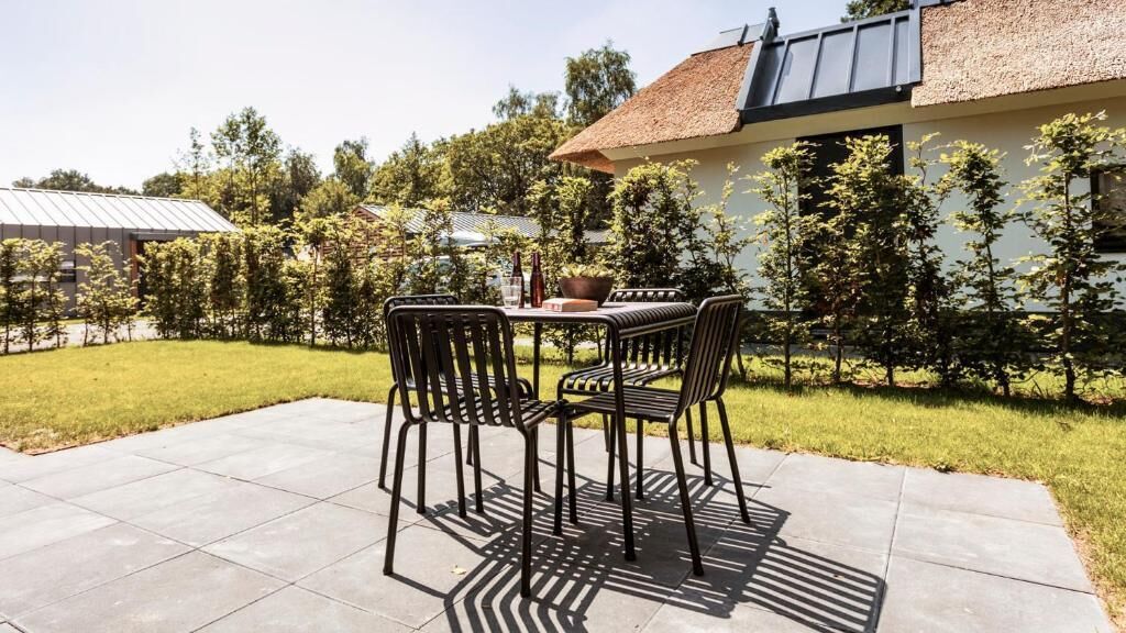 An outdoor patio with a table and chairs, surrounded by a well-maintained lawn and trees.
