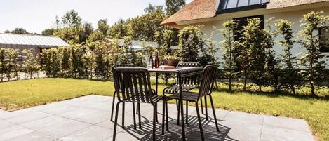 An outdoor patio with a table and chairs, surrounded by a well-maintained lawn and trees.