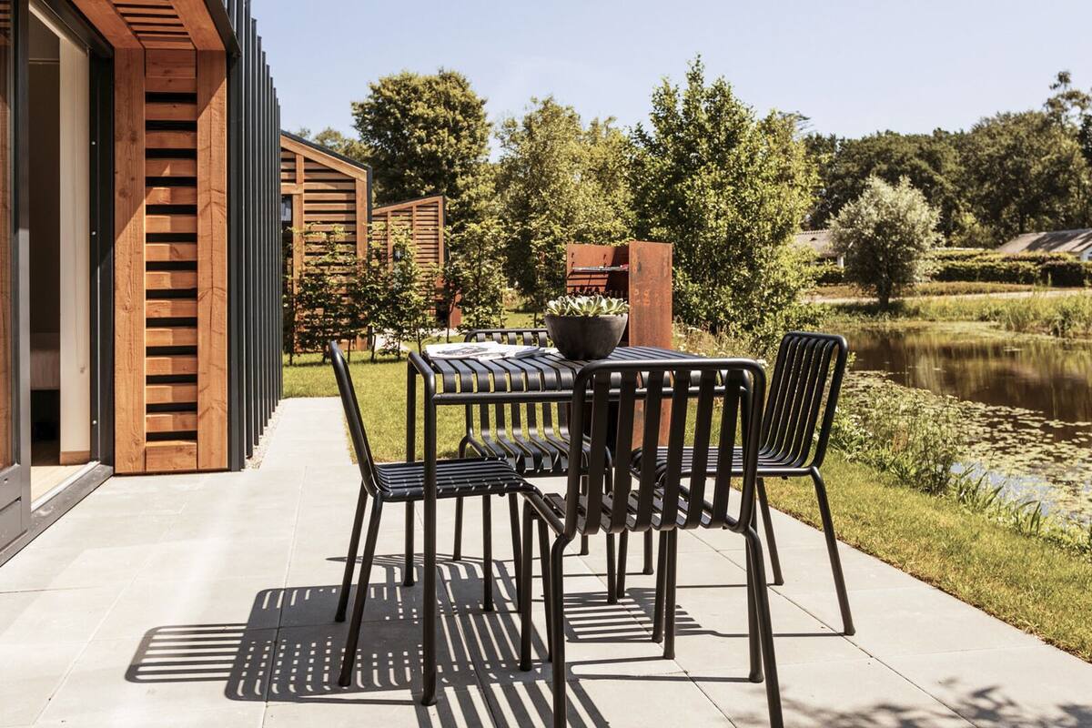 Une terrasse extérieure avec une table et des chaises, un pot de fleurs et une vue sur un étang.