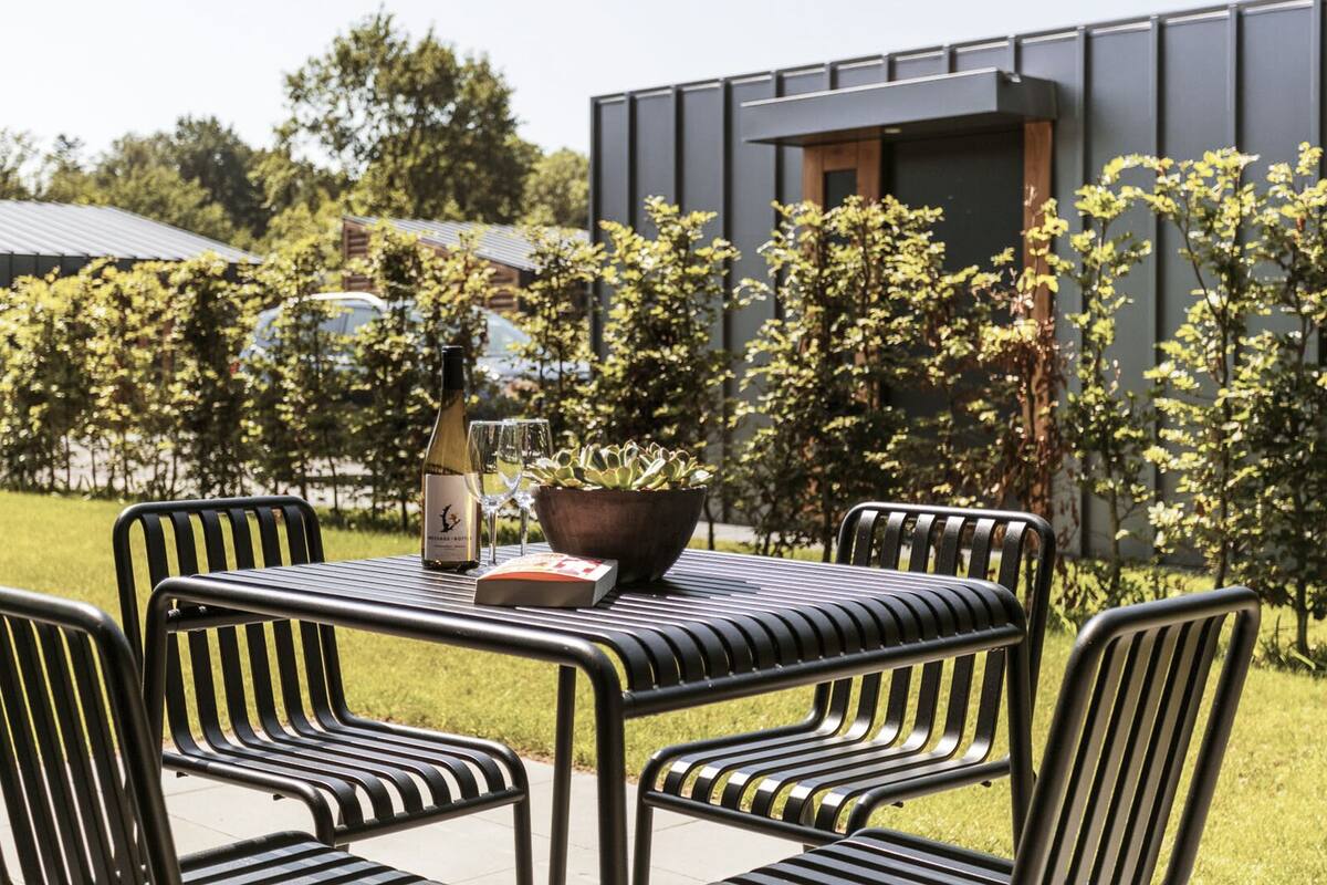Un espace extérieur aménagé avec une table et des chaises, une bouteille de vin et des verres.