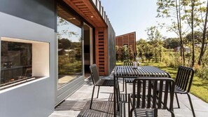 A modern outdoor patio with a dining table and chairs, surrounded by glass walls and wooden slats. - Suitelodges Gooilanden (Loosdrecht)