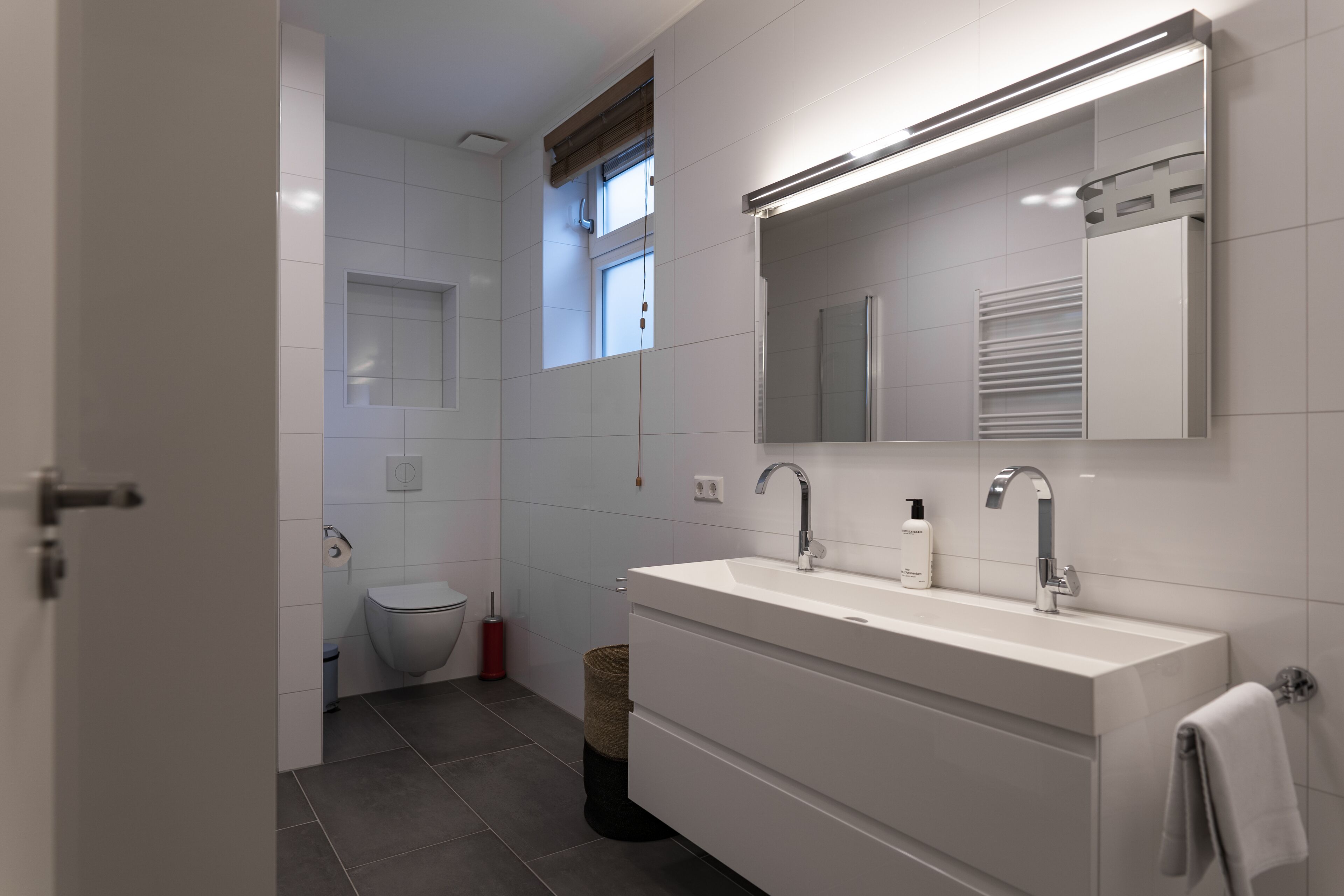 A modern bathroom with a double sink, a mirror, and a toilet.