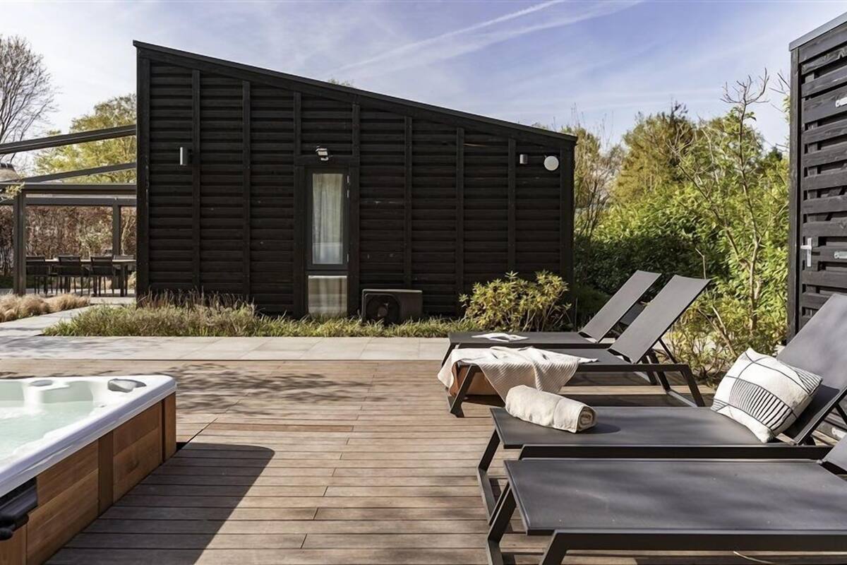 Une cabane moderne en bois, dotée d’un bain à remous, de chaises longues et d’un espace patio.