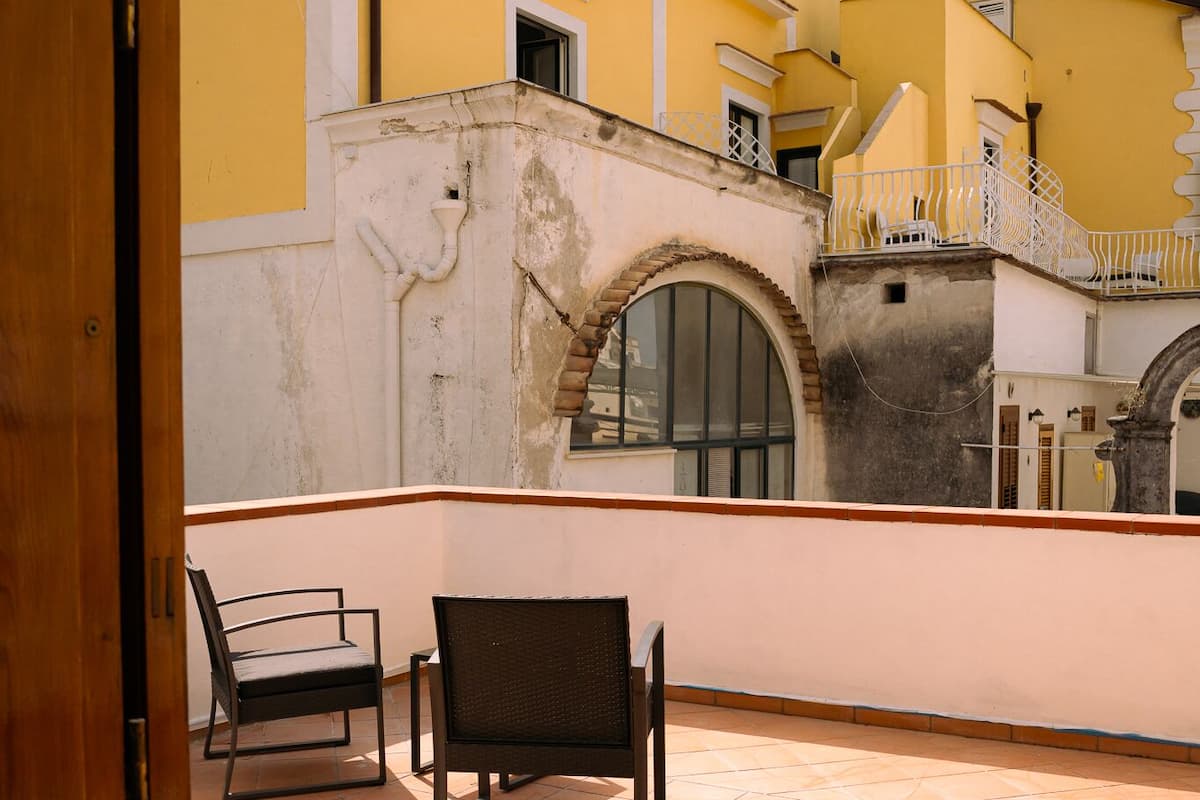 A balcony with two chairs, a tiled floor, and a yellow building with a white balcony railing in the background.